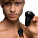 Young man holding a black vibrating silicone cock ring and its remote control against a white background.