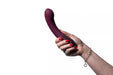 Hand holding a plum-colored Hot Octopuss Kurve G-spot vibrator with ergonomic curved design and control buttons visible.