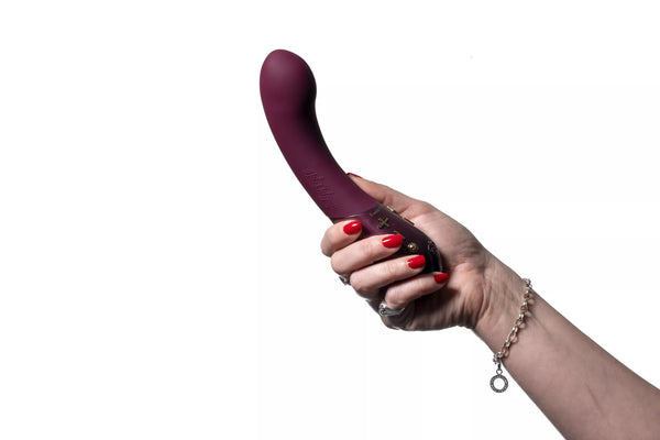 Hand holding a plum-colored Hot Octopuss Kurve G-spot vibrator with ergonomic curved design and control buttons visible.
