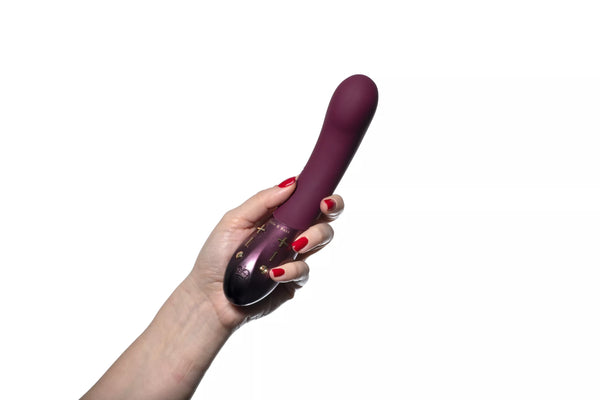 Hand holding a plum-colored Hot Octopuss Kurve G-spot vibrator with ergonomic shape and control buttons visible.