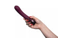 Hand holding a plum-colored Hot Octopuss Kurve G-spot vibrator with ergonomic shape and control buttons visible.
