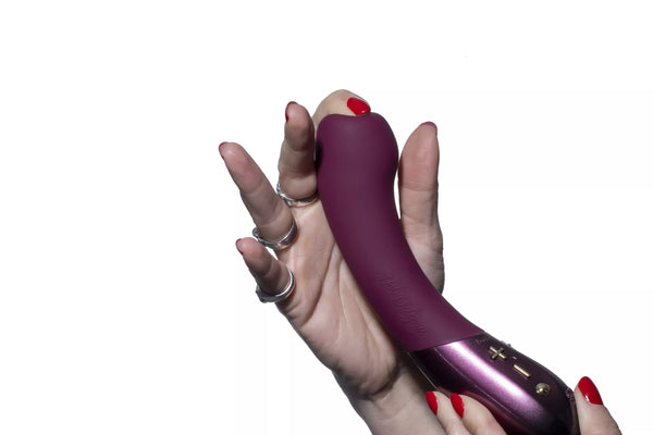 Hand holding a plum-colored Hot Octopuss Kurve G-spot vibrator with ergonomic shape and control buttons visible.
