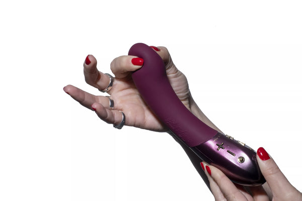 Hand holding a plum-colored Hot Octopuss Kurve G-spot vibrator with ergonomic shape and control buttons visible.