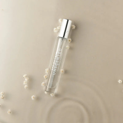 Clear glass bottle of Eye of Love Unscented Pheromone Perfume with silver cap on beige surface with small white flowers.