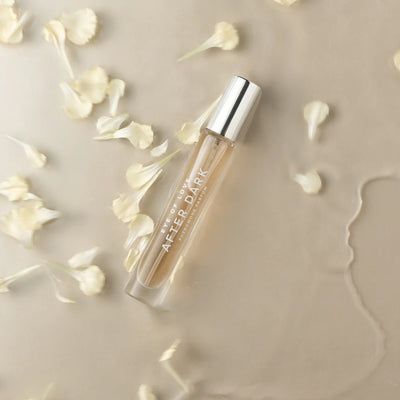 Eye of Love After Dark pheromone perfume in a sleek glass bottle with silver cap, surrounded by delicate white flower petals.
