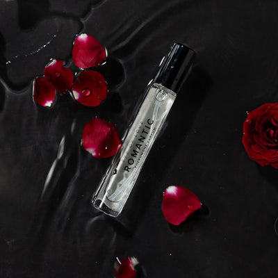 Eye of Love Romantic pheromone perfume bottle with scattered red rose petals on a dark wet surface.