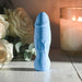 Blue silicone realistic vibrator with textured veins, standing upright beside white roses and a lit candle on a wooden surface.