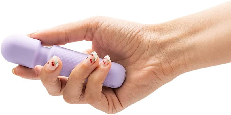 Hand holding a compact lavender Emojibator Tiny Wand vibrator with textured grip and rounded head.