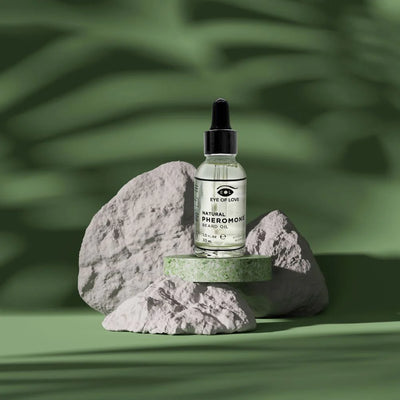 Eye of Love Natural Pheromone Beard Oil 30ml bottle with dropper on textured stones against a green background.