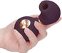 Hand holding a compact, dark purple clitoral vibrator with a rose gold button and a rounded, hollow silicone tip.