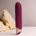 Sleek burgundy vibrator with smooth silicone body and rose gold base standing upright on a neutral surface with decorative stones.