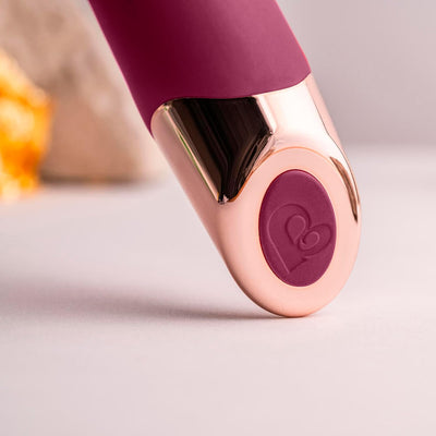 Close-up of the burgundy and rose gold Chaiamo vibrator with velvet touch silicone and heart-shaped button detail.