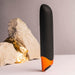 Sleek black and orange Chaiamo Burgundy vibrator standing upright with textured rocks and gold foil in the background.