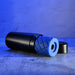 Black cylindrical case with a removable blue textured silicone stroker insert on a concrete surface with blue lighting.