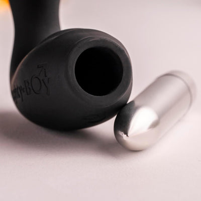Close-up of the black Naughty Boy prostate stimulator with its removable silver vibrating bullet on a light surface.
