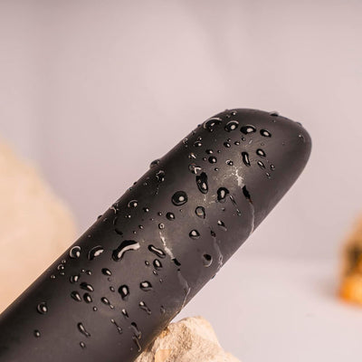 Close-up of the black Chaiamo Burgundy vibrator with water droplets highlighting its waterproof silicone surface.