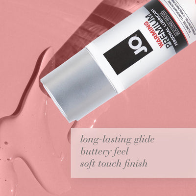 Jo Premium Warming Silicone Lubricant tube on pink surface with clear gel and text highlighting long-lasting glide and soft touch finish