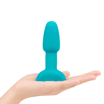 Compact turquoise silicone vibrating rimming plug shown resting on an open hand for size reference.