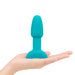 Compact turquoise silicone vibrating rimming plug shown resting on an open hand for size reference.
