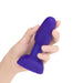 Hand holding a compact, smooth purple silicone anal plug with a flared base and rounded tip.