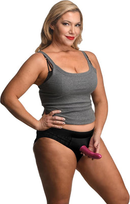 Woman wearing black lace crotchless panty harness with attached purple strap-on, paired with gray tank top.