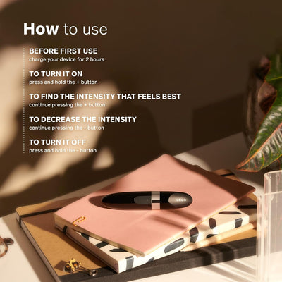 LELO Mia 2 compact black massager resting on stacked notebooks with usage instructions in soft natural light.