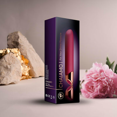 Chaiamo Burgundy vibrator packaging displayed with decorative rocks and a pink flower on a soft beige background.