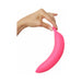 Hand holding a curved pink silicone vibrator shaped like a banana against a white background.