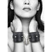 Black bonded leather wrist cuffs with metal chain and plush lining worn on model's wrists against a white background.