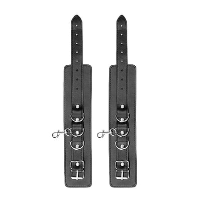 Pair of black leather adjustable wrist or ankle cuffs with metal buckles and D-ring connectors.