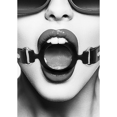 Close-up black and white image of a person wearing a black silicone ring gag with adjustable leather straps and metal clasps.