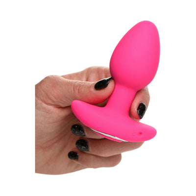 Hand holding a bright pink silicone butt plug with a wide base and smooth, tapered design.
