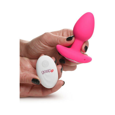 Hand holding a vibrant pink silicone butt plug and a white remote control with the Gossip logo on a white background.