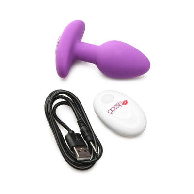 Vibrant violet silicone butt plug with wide base, white remote control, and black USB charging cable on white background.