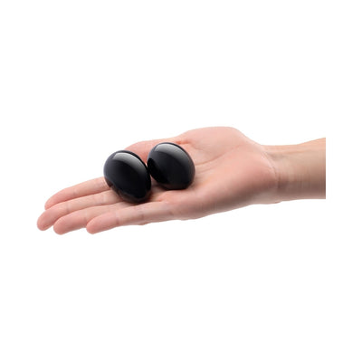 Hand holding two smooth black obsidian yoni eggs with a glossy finish on a white background