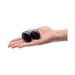 Hand holding two smooth black obsidian yoni eggs with a glossy finish on a white background