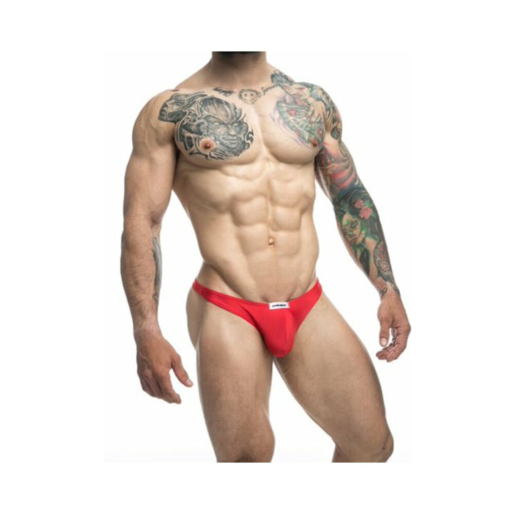 Muscular male model wearing red Malebasics Justin + Simon Classic Tanga underwear with tattooed arms and chest.