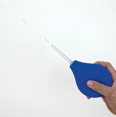 Hand holding a blue 11 oz bulb douche with a translucent nozzle spraying water against a white background.