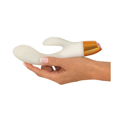 Hand holding a white and gold You2toys Glow-in-the-dark Rabbit Vibrator with textured tip and dual stimulation design.