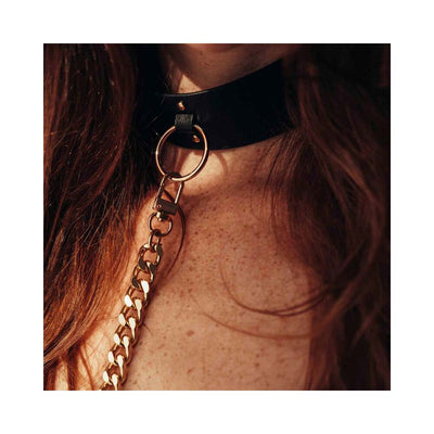 Close-up of a black vegan leather choker with gold chain leash worn around the neck.