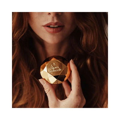 Close-up of a woman holding a gold faceted Bijoux Indiscrets Twenty One Vibrating Diamond in front of her lips.