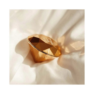 Golden faceted diamond-shaped clitoral vibrator resting on soft white fabric with subtle shadows.