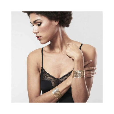Woman wearing black lace lingerie with gold metallic mesh handcuff bracelets on her wrists against a plain background.