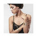 Woman wearing black lace lingerie with gold metallic mesh handcuff bracelets on her wrists against a plain background.