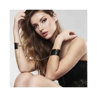 Woman wearing black metallic mesh handcuff bracelets connected by a gold chain, styled with elegant makeup and lace outfit.