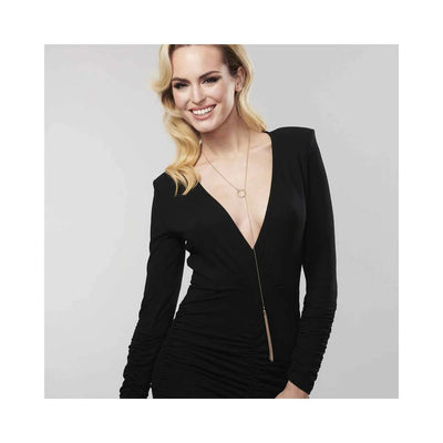 Smiling woman wearing a black deep V dress and a gold Magnifique Tickler Pendant necklace with a mini-whip design.