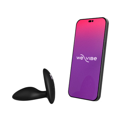 Black silicone vibrating anal plug next to smartphone displaying We-Vibe app interface on white background.