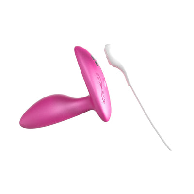 Pink silicone We-Vibe Ditto+ vibrating anal plug with remote control and USB charging cable on white background.