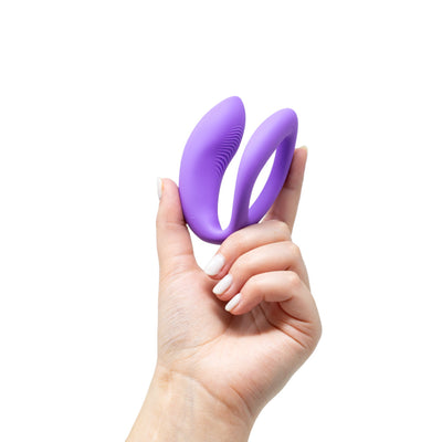 Hand holding a compact purple We-Vibe Sync O couples vibrator with a flexible O-shaped design.