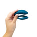 Hand holding a blue We-Vibe Sync O couples vibrator with a flexible O-shaped design against a white background.
